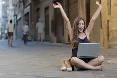 a woman sitting on the ground with her laptop in front of her and arms up