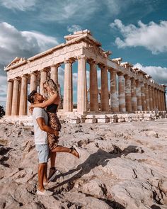 two people standing in front of the parthenon on top of a rocky hill