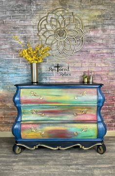 a painted dresser with flowers on top and a brick wall behind it in the background