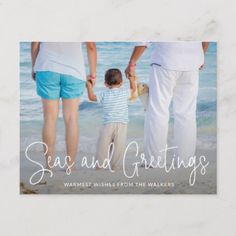 a man and woman holding hands with a small child on the beach near the ocean