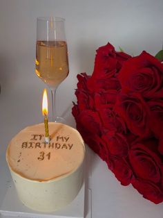 a birthday cake with a candle on it next to a bouquet of roses and a glass of wine