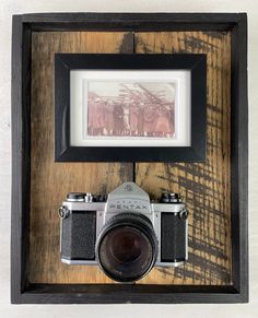 an old fashioned camera sitting on top of a wooden table next to a framed photograph