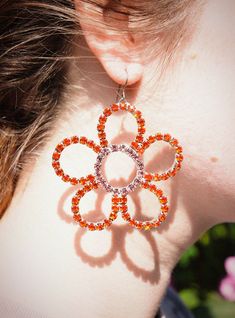 The Glam Daisy Mismatched Earrings feature two colors of super sparkly rhinestone, and are a fun statement piece for going out or spicing up jeans and a tee. One has a pink center with orange petals, the other has an orange center with pink petals for a subtle mismatched look. Each pair is handmade with love and may slightly vary in shape from what is pictured. Each flower measures approximately 2.4" x 2.4" x .2" / 6cm x 6cm x 44cm. Length: 3" / 7.5 cm. Composition: Nickel-free, raw titanium fre Orange Flower Earrings For Party, Orange Flower Shaped Earrings For Party, Sparkling Flower Earrings For Party, Trendy Orange Jewelry For Spring, Mismatched Earrings, Pink Petals, Orange And Pink, Handmade With Love, Statement Pieces