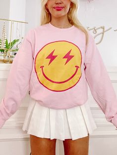 Our Striking Smiles Crewneck is a light pink pretty that is super soft inside! The front has a large smiley face with lightning bolt eyes. Also available in a tee. Casual Winter Tops With Smiley Face, Casual Smiley Face Winter Tops, Trendy Fall Tops With Smiley Face, Trendy Smiley Face Tops For Fall, Trendy Fall Smiley Face Tops, Crew Neck Top With Smiley Face For Winter, Casual Pink T-shirt With Smiley Face, Winter Crew Neck Top With Smiley Face, Fun Pink Tops With Smiley Face