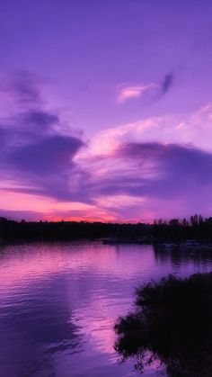 the sky is purple and there are clouds in the sky over the water at sunset