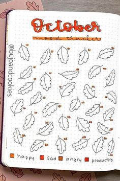 an open notebook with leaves on it and the words october written in orange ink next to two