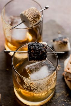 two glasses filled with ice and some food on top of a wooden table next to crackers