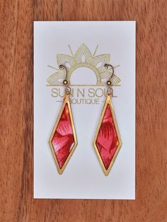 a pair of red and gold earrings sitting on top of a card