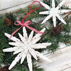 two snowflakes are hanging on a wooden table with pine cones and twine