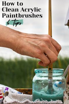 a person using a paintbrush to clean acrylic paints in a glass jar