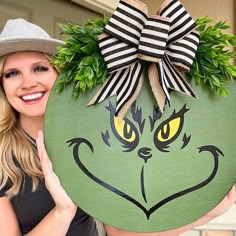 a woman is holding up a green grin face painted on an egg with a bow