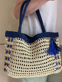 a woman holding a crocheted blue and white bag with tassels on it