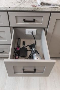 an open drawer in the middle of a kitchen with various electrical cords and plugs