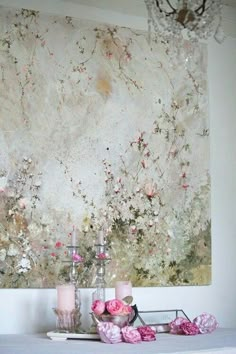 a table with candles and flowers on it in front of a wall hanging art piece