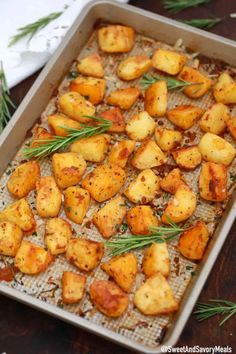 roasted potatoes with rosemary sprigs in a baking pan on a wooden table, ready to be cooked