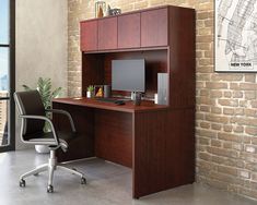 an office desk with a computer on it in front of a brick wall