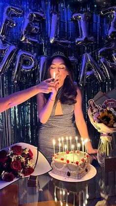 a woman standing in front of a cake with lit candles on it while another woman blows out the candles