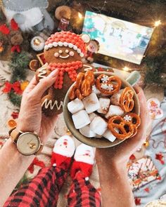 a person holding a bowl filled with pretzels, marshmallows and ginger cookies