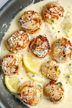 a pan filled with cooked scallops covered in sauce and garnished with lemon wedges