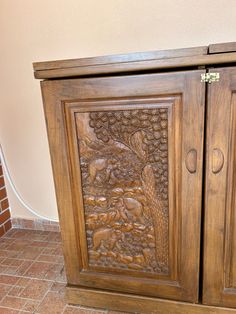 a wooden cabinet with carvings on the front and side doors, sitting on a tile floor