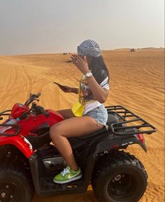 a woman riding on the back of an atv in the middle of sand dunes with her hand up to her face