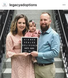 a man and woman holding a sign with a baby on it in front of some stairs