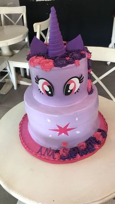 a purple cake with pink frosting and an unicorn face on top, sitting on a table