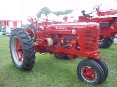 an old red farmall tractor parked in the grass at a show or sale with other antique tractors behind it