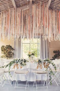 the table is set up for a wedding reception with white chairs and flowers on it