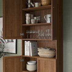 a wooden cabinet with wine glasses, plates and other items on the shelves in front of it