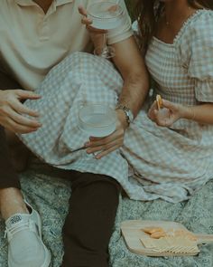 a man and woman sitting next to each other on top of a bed holding cups