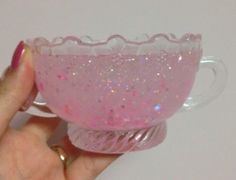 a hand holding a pink glass cup with glitter on the rim and bottom, in front of a white background