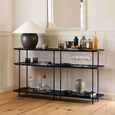 a shelf with wine glasses and bottles on it in front of a wall mounted mirror