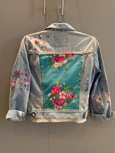 a denim jacket with flowers painted on it hanging from a hook in a room next to a wall