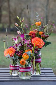 three vases filled with flowers sitting on top of a wooden table in the grass