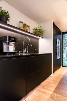 a modern kitchen with black cabinets and wood flooring on the walls, along with potted plants