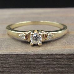 a yellow gold ring with three stones on it sitting on top of a wooden surface