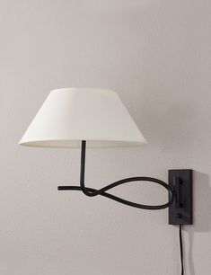 a lamp that is plugged into the side of a wall mounted light with a white shade on it