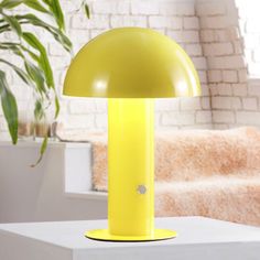 a yellow lamp sitting on top of a white table next to a potted plant