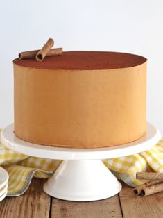 a cake with cinnamon on top sitting on a white plate next to some cinnamon sticks