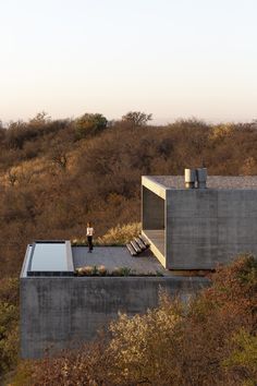 a person standing on the roof of a building in front of trees and bushes with a sky background