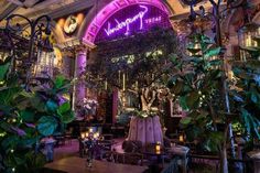 the interior of a restaurant with purple lighting and greenery in front of an archway