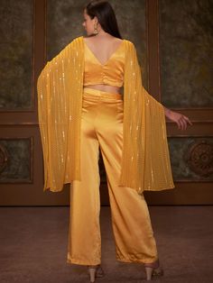 This is a two-piece Yellow Butterfly Drape Top Set from the Suruchi Parakh collection. The yellow butterfly twisted drape top in georgette is paired with satin silk straight pants. The butterfly style crop top has a back hook opening. There is beautiful sequin thread work all over the crop top. The yellow color with sequin, padding and long drape enhances the graceful, drape top set. Silk V-neck Party Sets, Satin Party Wear Sets, Elegant Party Pant Set With Cape Sleeves, Festive Crop Top For Night Out, Silk Palazzo Set For Evening, Silk Draped Party Set, Fitted Palazzo Set With Cape Sleeves For Party, Summer Party Palazzo Set With Cape Sleeves, Festive Yellow Pant Set For Party