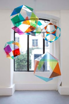 several colorful kites hanging from the ceiling in front of a window with white walls