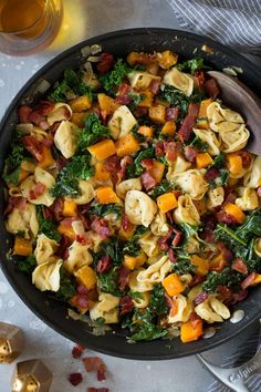 a skillet filled with pasta, bacon and spinach on top of a table