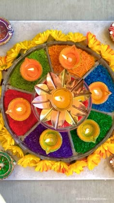 an arrangement of colorful candles and flowers on a table with other items around the perimeter