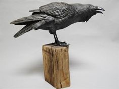 a statue of a crow sitting on top of a piece of wood with it's wings spread