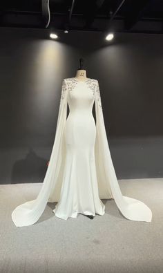 a white wedding dress with long sleeves and a cape on display in a dark room