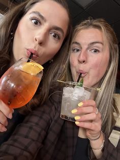 two women are drinking drinks together at a bar and posing for the camera with their mouths open