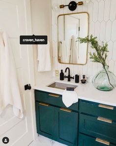 a white bathroom with green cabinets and gold trim on the mirror above the sink is a vase filled with greenery